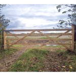 Charltons Forester wooden gate with 5 bars hung across a field entrance with metal hinges and latching bolt.